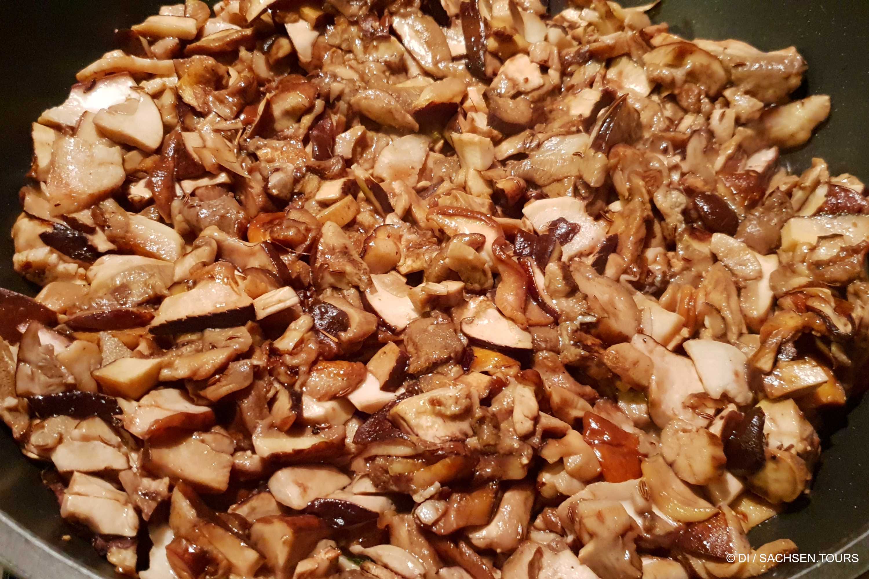 Nahaufnahme zerkleinerter Pilze mit verschiedenen Braun- und Cremetönen, die zum Braten in einer Pfanne vorbereitet werden.