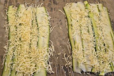 Zwei Gruppen von dünn geschnittenen Zucchinistreifen werden flach auf Pergamentpapier ausgelegt und jeweils mit einer großzügigen Menge an geriebenem Käse belegt, so dass eine sandwichartige Schicht entsteht, die gekocht oder gebacken werden kann.