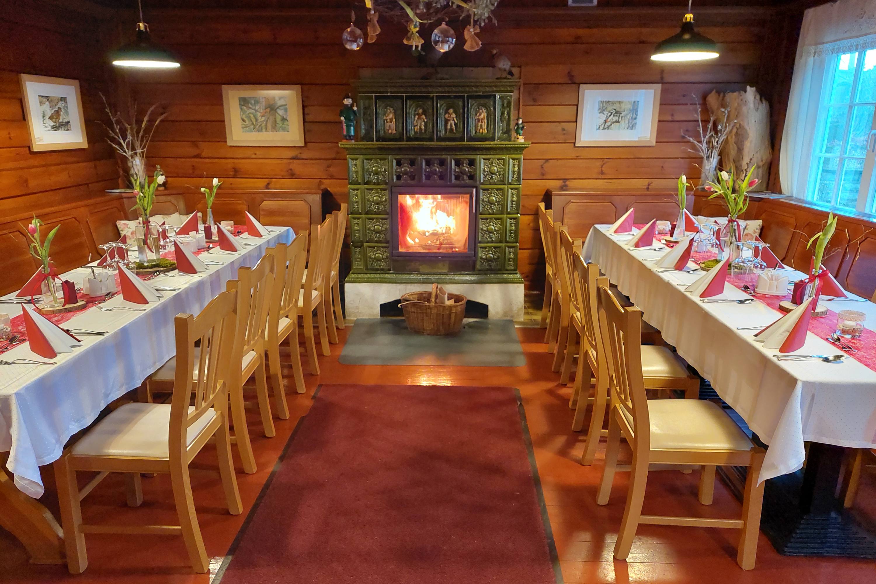 Im Berggasthof Czorneboh gibt es einen gemütlichen Gastraum mit Holzwänden und zwei langen Tischen, an denen das Essen serviert wird - mit weißen Tischtüchern, roten Servietten und Blumenschmuck. Ein grün gekachelter Kamin, in dem ein Feuer brennt, wärmt das Ende des Raums.